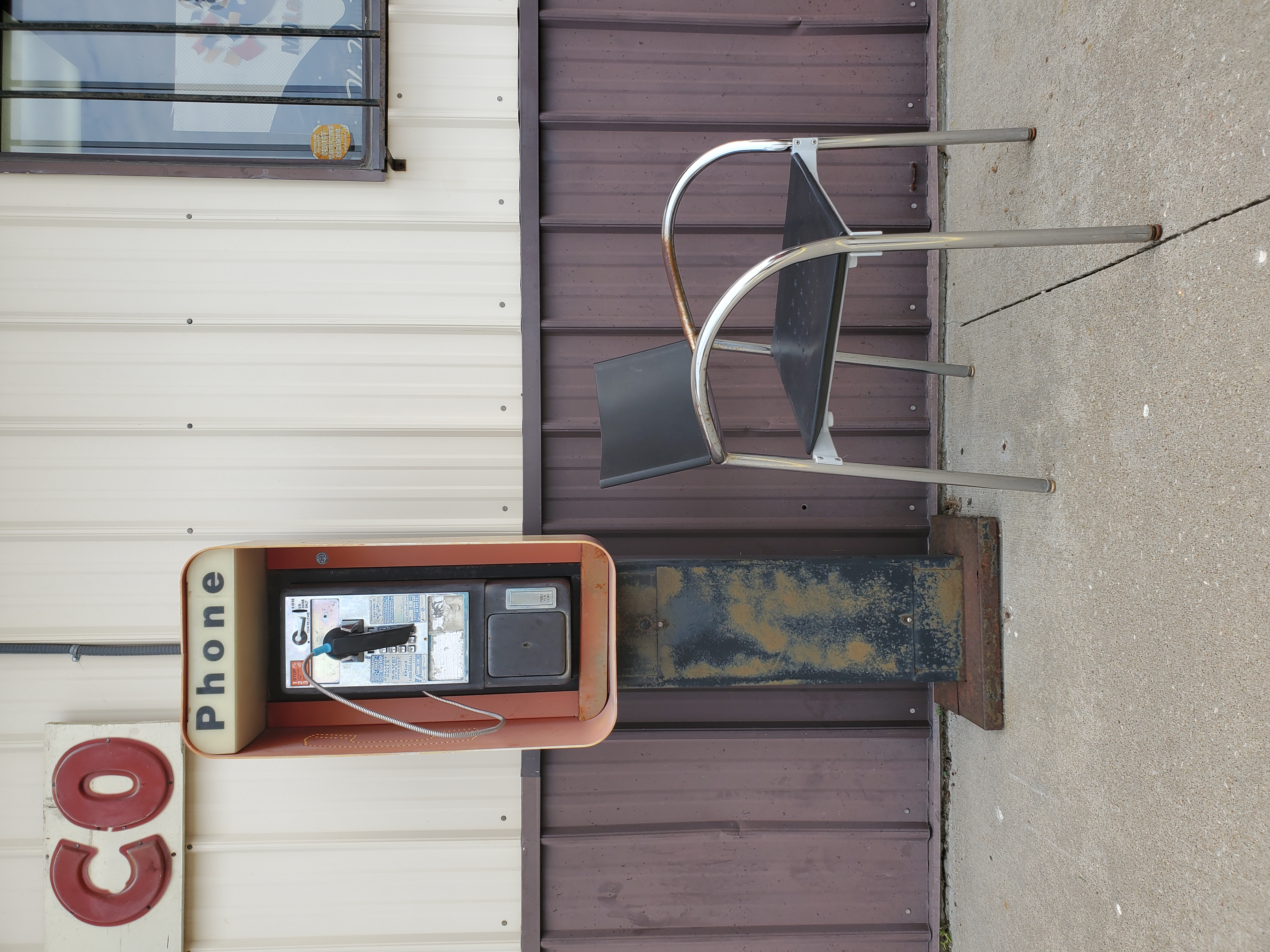 Image with an old pay phone next to a rusted chair