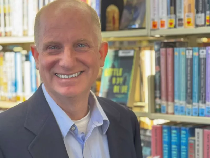 John Greifzu standing in front of shelves of books